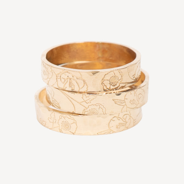 Three stacked gold rings with engraved floral patterns, displayed on a clean off-white background.