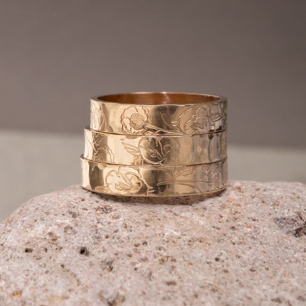 A gold band ring with a hammered texture and engraved floral patterns, shown on a light gray background.