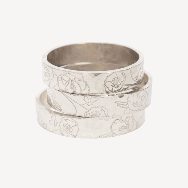 Three stacked silver rings with a hammered texture and engraved floral patterns, shown on a light gray background.