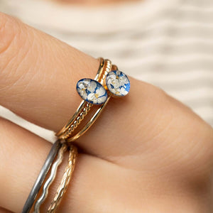 Close-up of a hand wearing two rings with floral heart-shaped stones on a neutral background