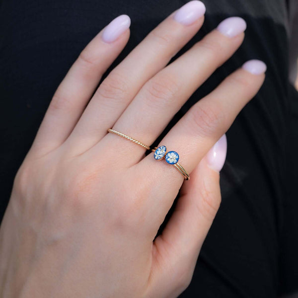 Hand wearing a gold ring with blue gemstones against a black background