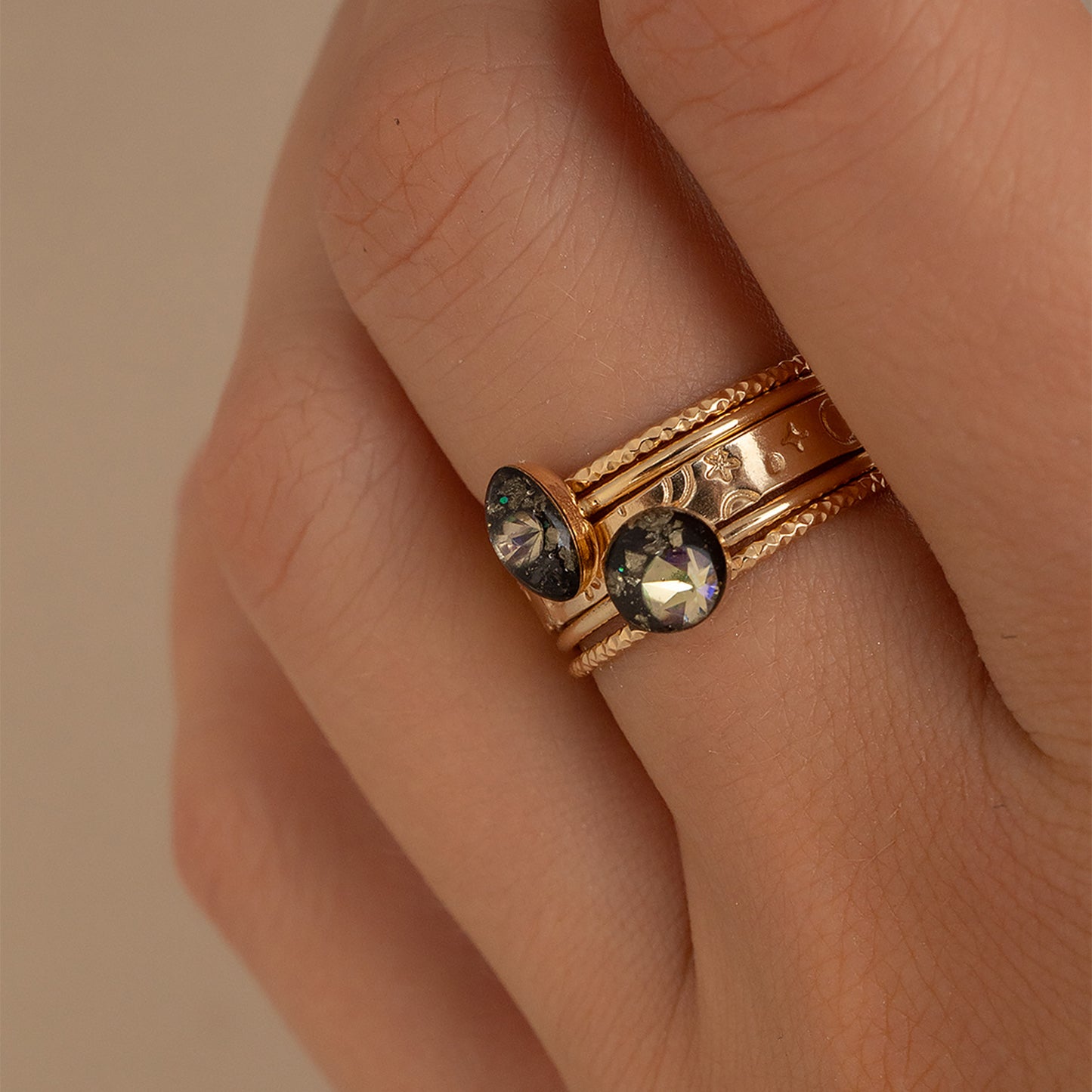 Gold ring with gemstones on a person's finger against a beige background