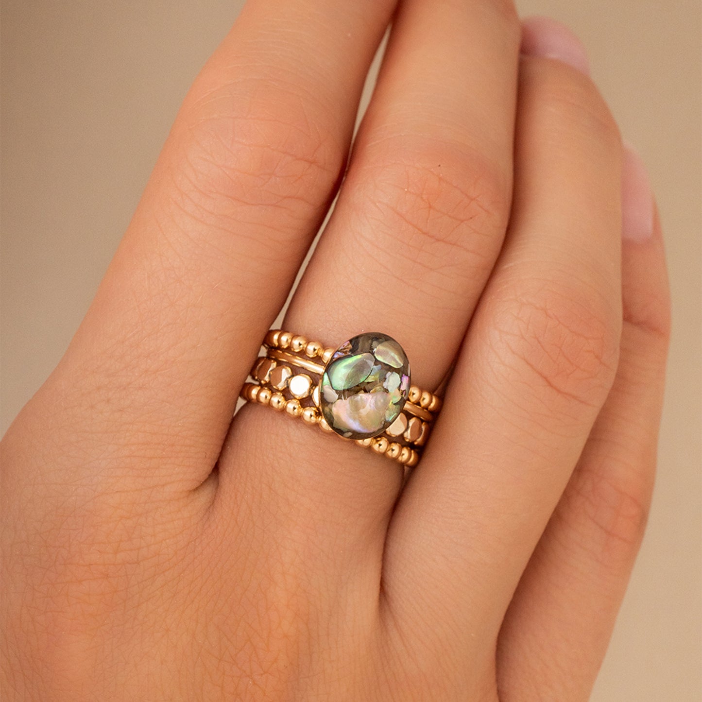 Gold ring with a central gemstone on a person's finger against a beige background