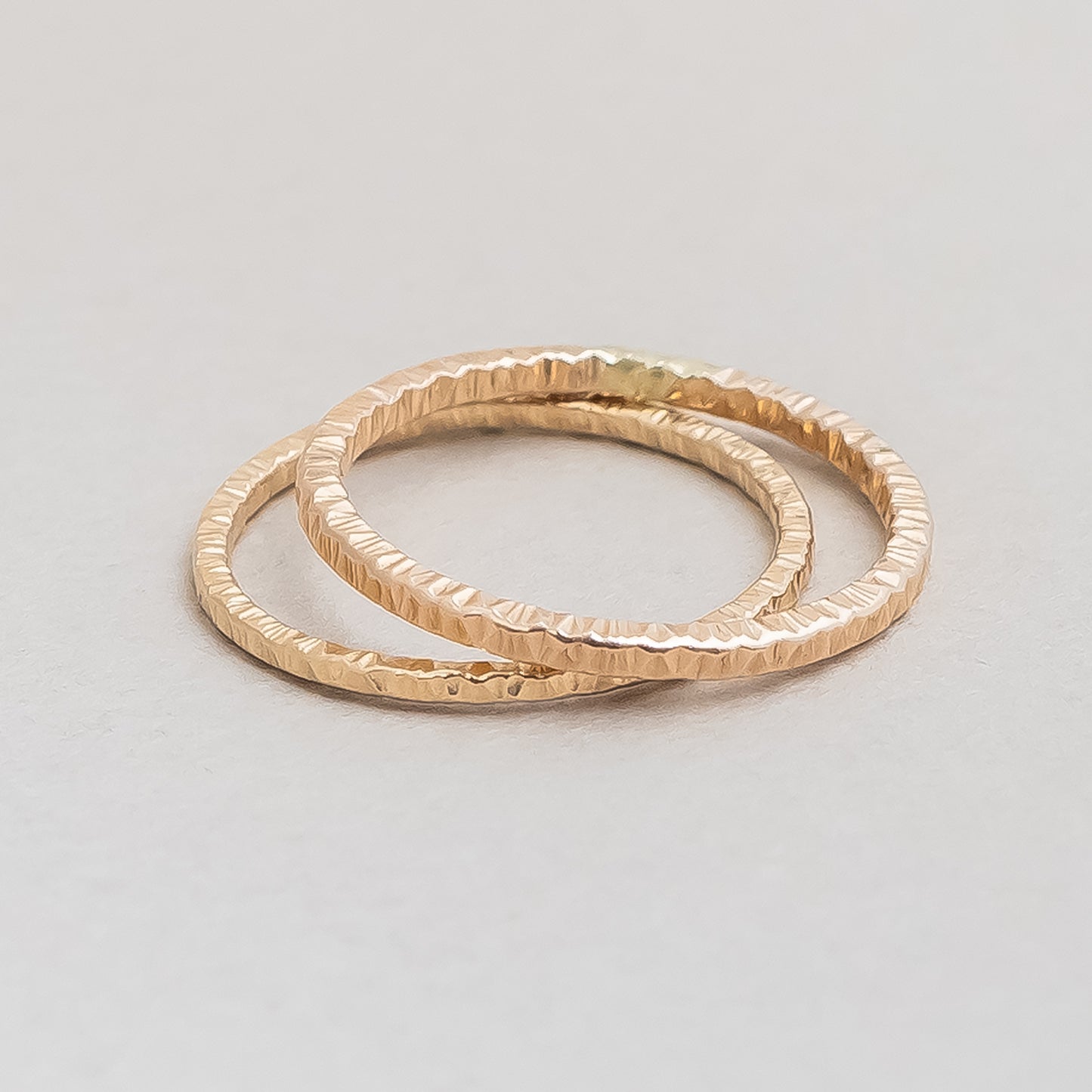 Two gold rings with textured surfaces on a light gray background