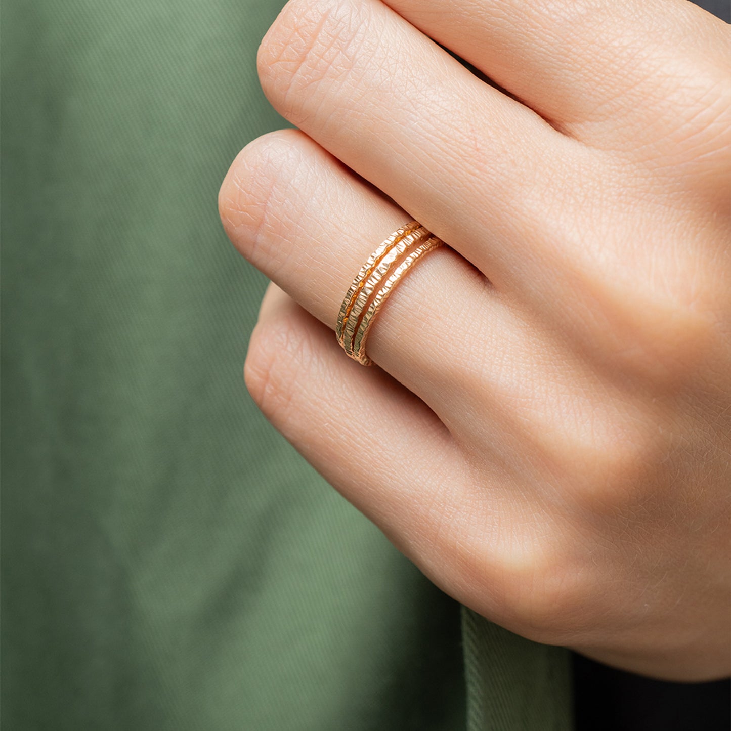 Close-up of a hand wearing a gold ring on a green background