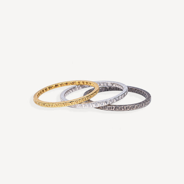 Three textured bangles in gold, silver, and white gold, overlapping on a light off-white background.