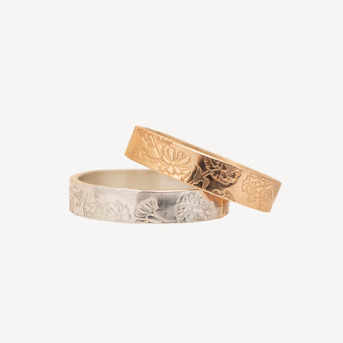 Two engraved rings, one in polished yellow gold and one in silver, displayed overlapping on a clean off-white background.