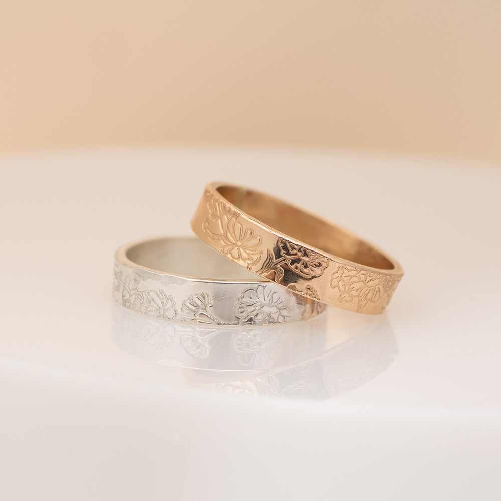 Two engraved rings, one in polished yellow gold and one in silver, displayed overlapping on a clean off-white background.