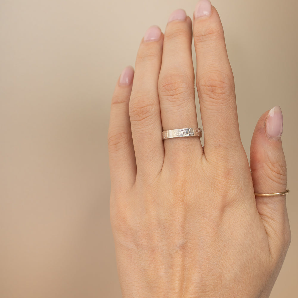 Two engraved metal bands, one rose gold and one silver, overlapping on a clean off-white background. Both bands feature a floral pattern engraved on the outer surface.