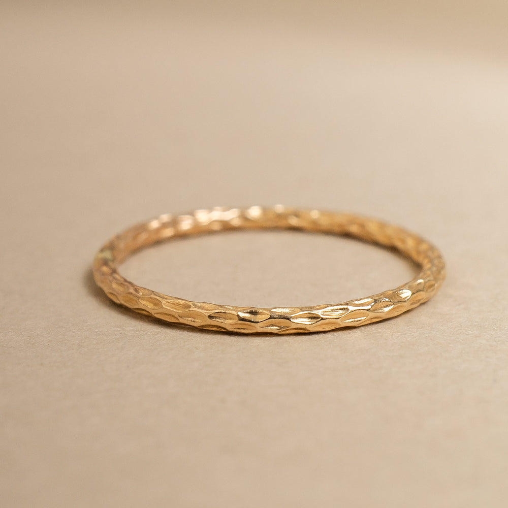 
                      
                        Gold ring with textured design on a beige background
                      
                    
