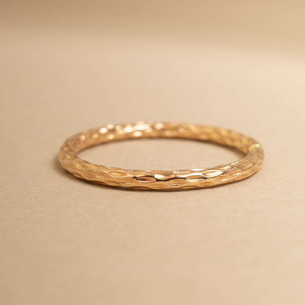 
                      
                        Gold ring with textured design on a beige background
                      
                    
