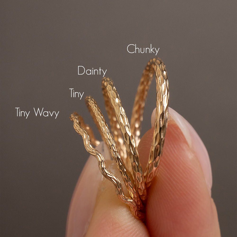 Gold rings labeled 'Tiny Wavy', 'Dainty', 'Chunky' held by a hand against a dark background.