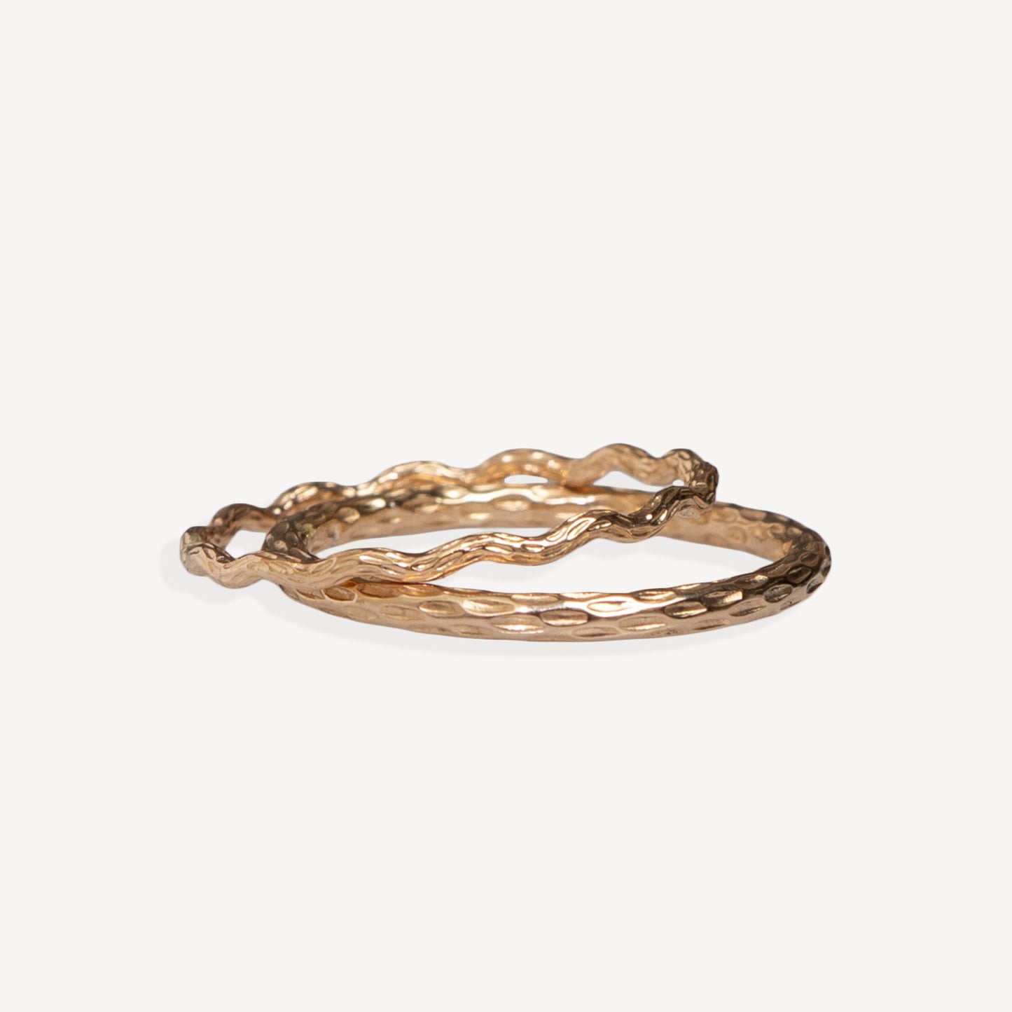 Two overlapping hammered metal rings in a warm gold tone, photographed on a clean off-white background.