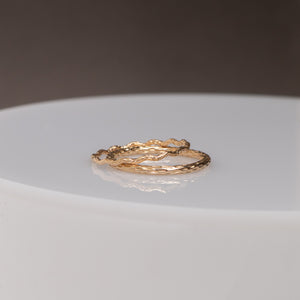 Two textured gold rings with organic, wavy shapes resting on a white circular pedestal against a dark gray background.
