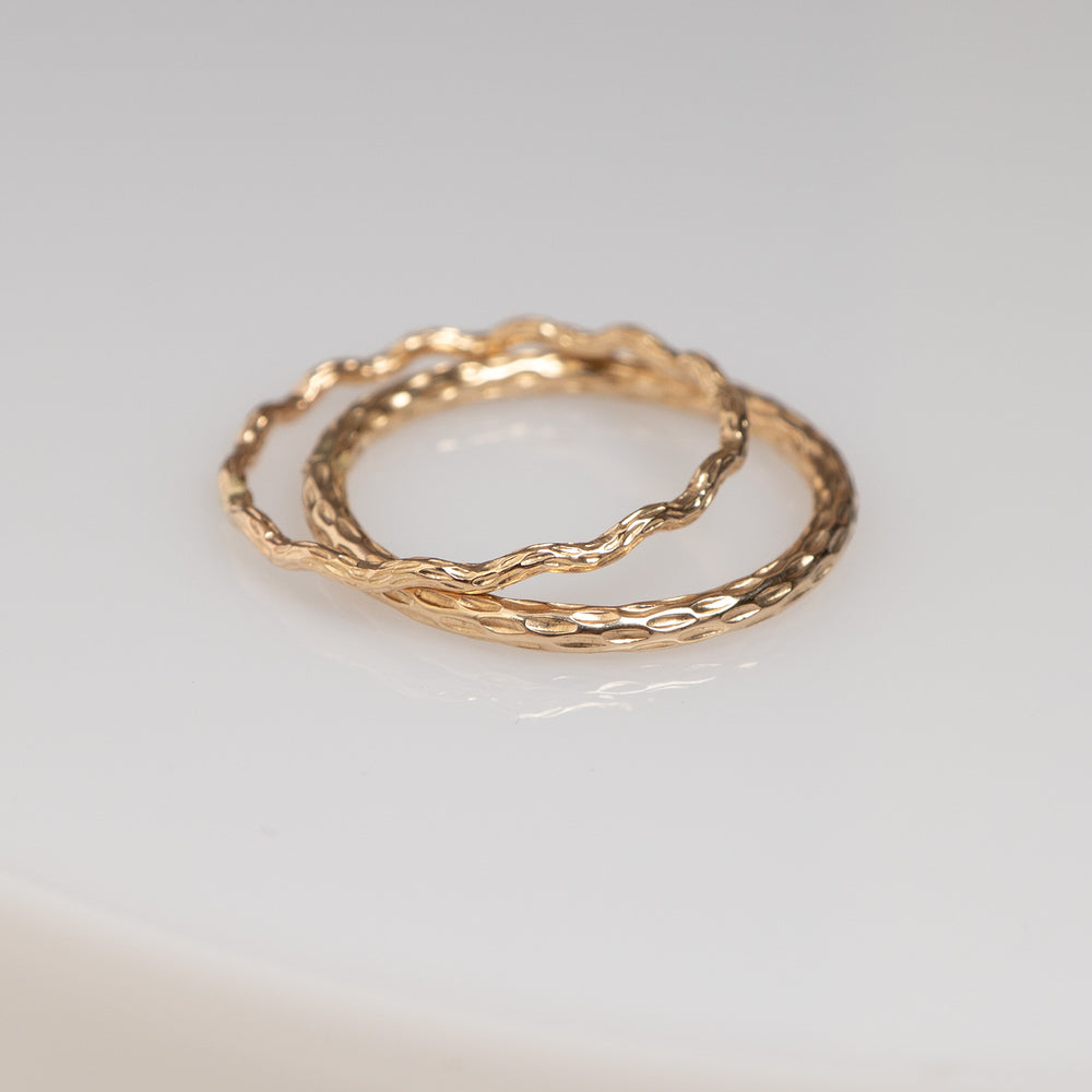 Two overlapping hammered metal rings in a warm gold tone, photographed on a clean off-white background.