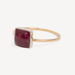 A square-cut deep red ruby gemstone ring set in a polished gold band, photographed on a clean, light off-white background.