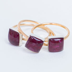 Three gold rings with square-cut deep purple gemstones in silver bezel settings, arranged on a white background.