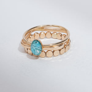 A gold-plated double-band ring featuring a central oval-cut light blue gemstone and a row of small gold beads on the outer band, set against a plain light gray background.