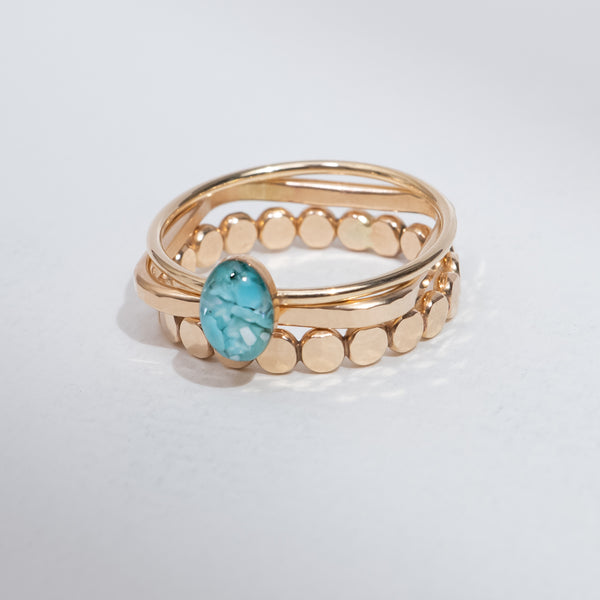 A gold-plated double-band ring featuring a central oval-cut light blue gemstone and a row of small gold beads on the outer band, set against a plain light gray background.