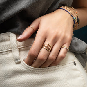 Hand wearing gold rings with bracelets on a neutral background