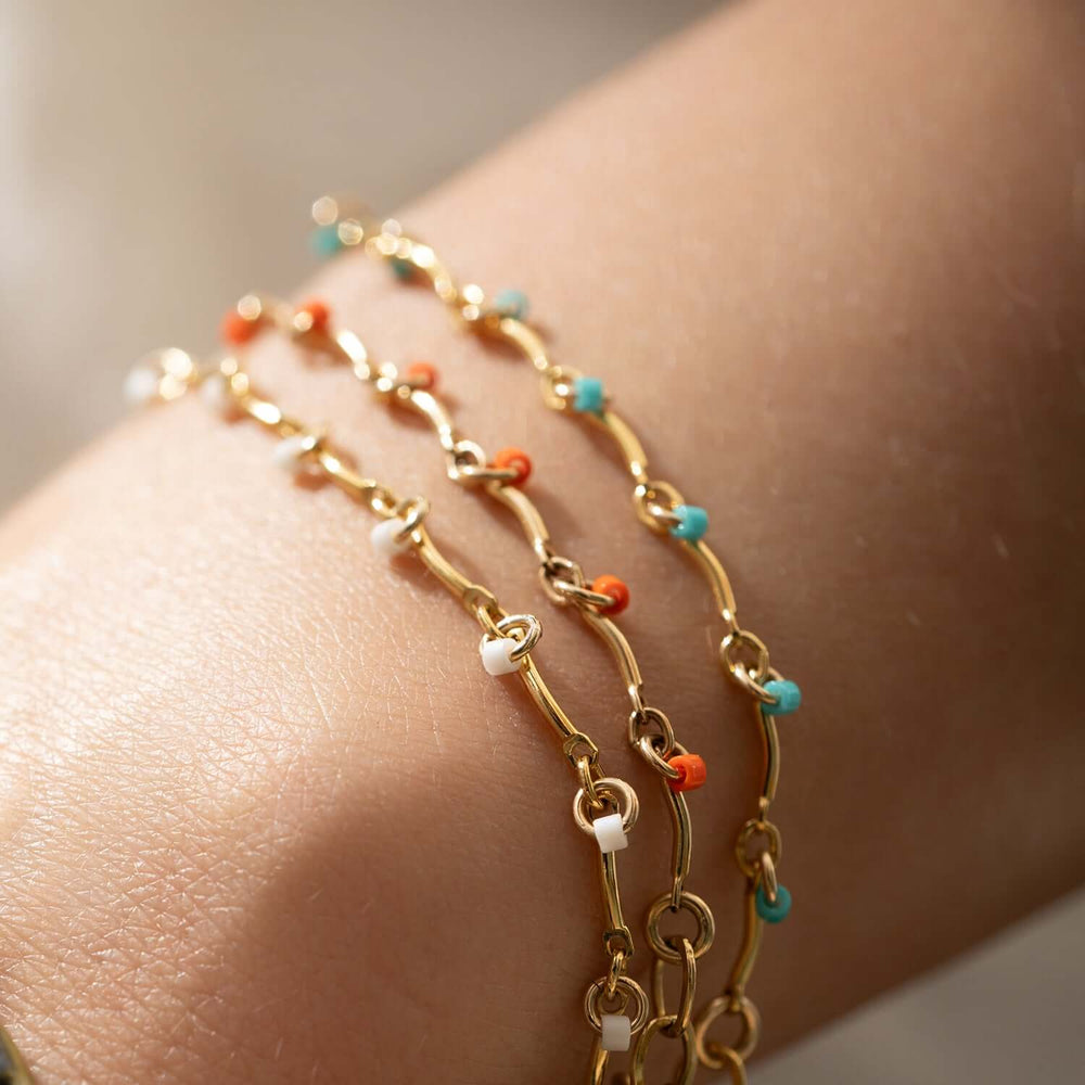Gold bracelet with small orange beads on a white background