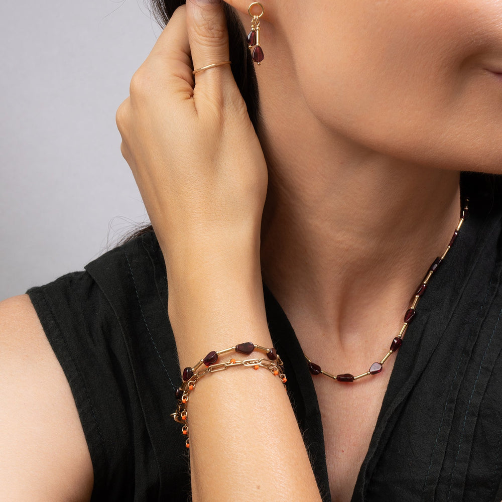 A gold chain necklace featuring faceted dark red Garnet beads, displayed on a clean off-white background.