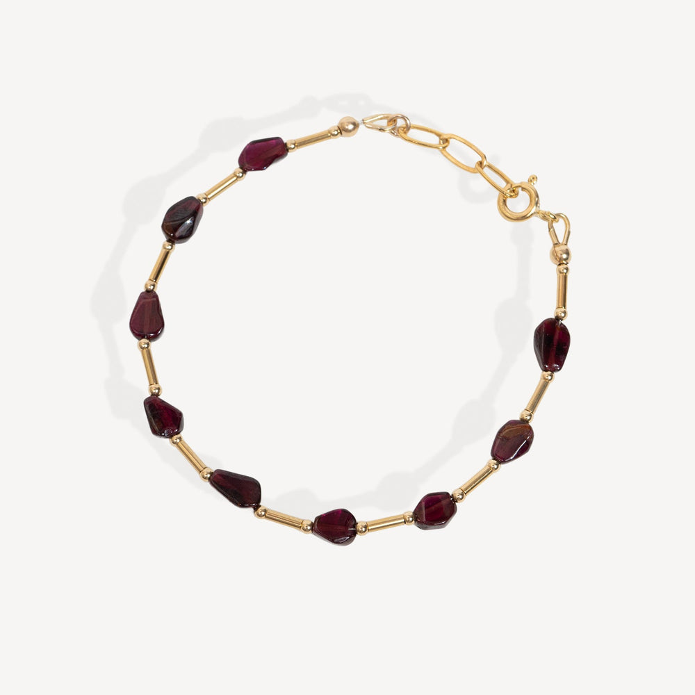 A gold chain necklace featuring faceted dark red Garnet beads, displayed on a clean off-white background.