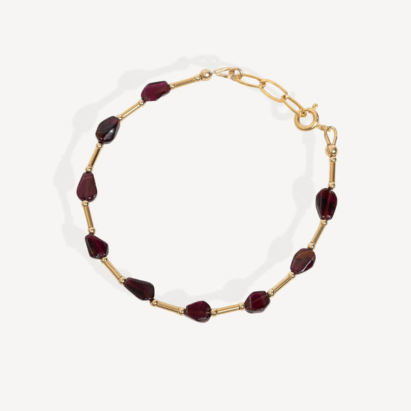 A gold chain necklace featuring faceted dark red Garnet beads, displayed on a clean off-white background.
