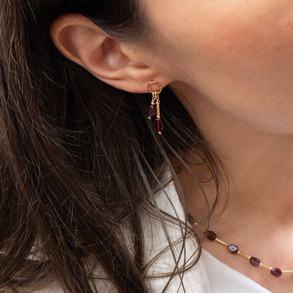 A pair of gold drop earrings with teardrop-shaped Garnet gemstone, shown on a light gray background 