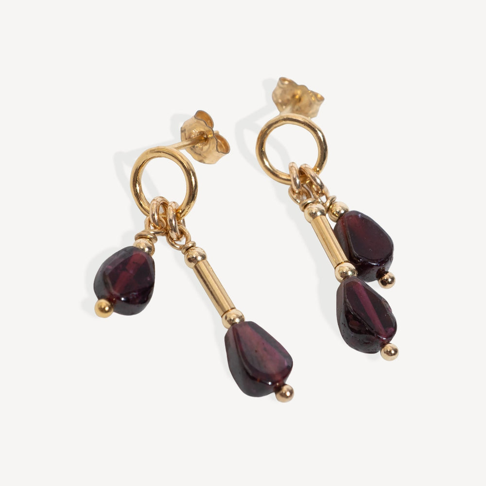 A pair of gold drop earrings with teardrop-shaped Garnet gemstone, shown on a light gray background 