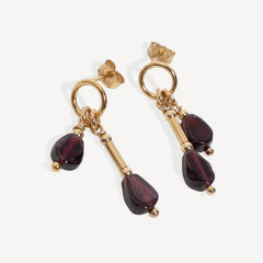 A pair of gold drop earrings with teardrop-shaped Garnet gemstone, shown on a light gray background 