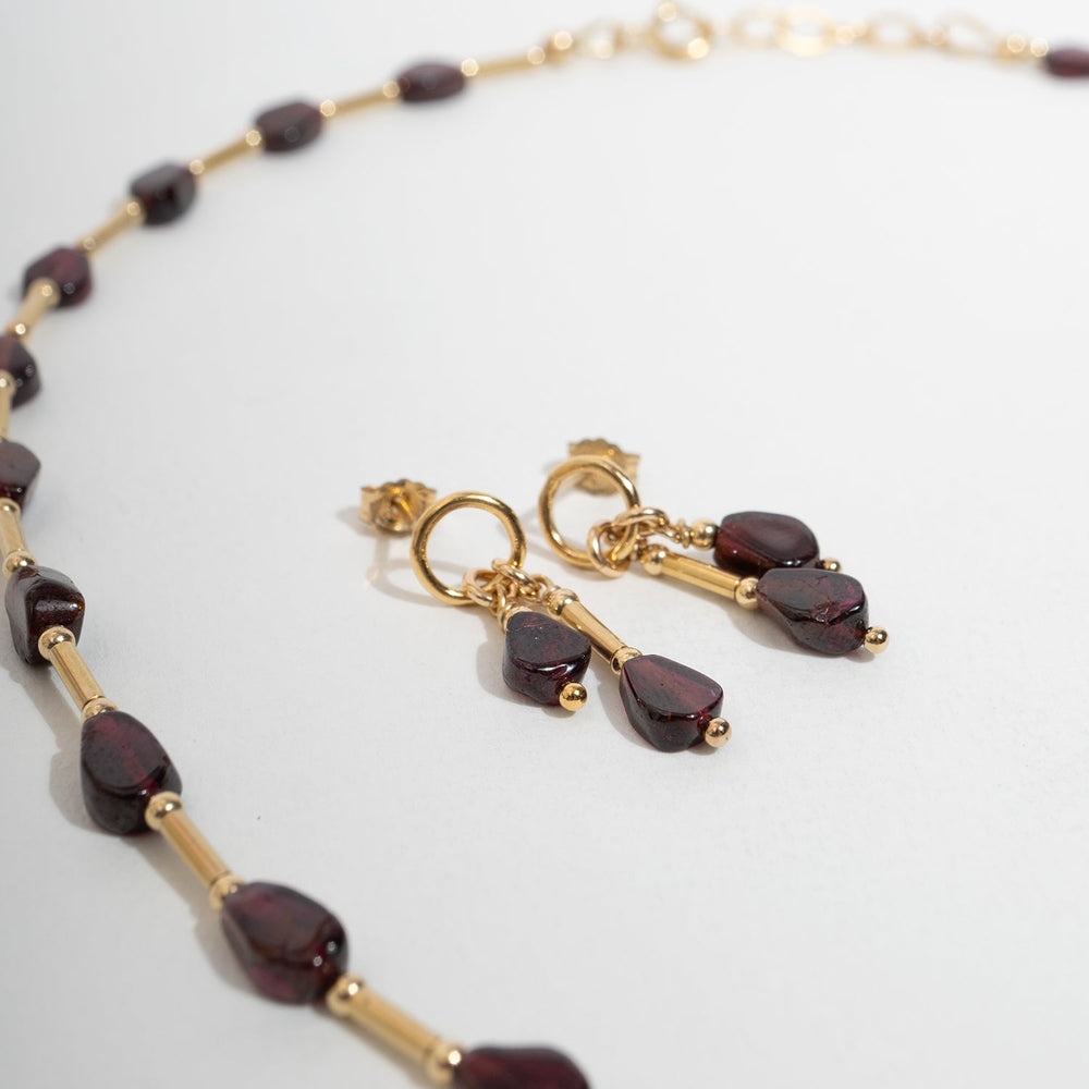 A pair of gold drop earrings with teardrop-shaped Garnet gemstone, shown on a light gray background 