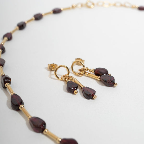 Gold-tone jewelry set featuring a beaded necklace and matching drop earrings with dark burgundy teardrop-shaped Garnet beads, displayed on a clean white surface.