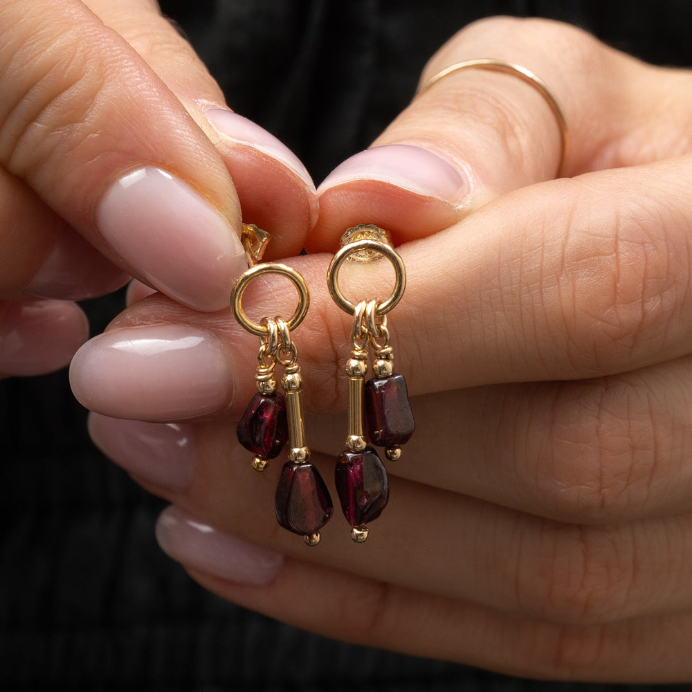 A pair of gold drop earrings with teardrop-shaped Garnet gemstone, shown on a light gray background 