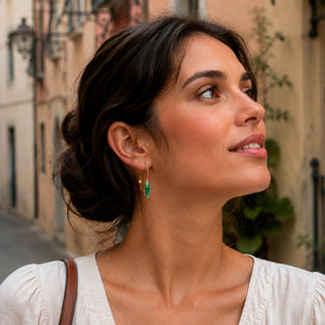 Woman with a bun hairstyle and green earrings looking to the side on a street.