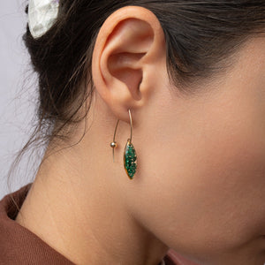 Close-up of an ear wearing a green earring with a neutral background