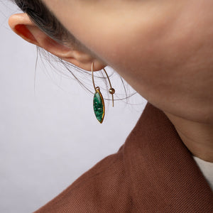 Close-up of a person wearing a green leaf-shaped earring on a plain background