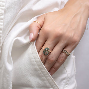Hand wearing a ring with a green gemstone on a white background