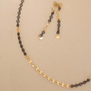 Gold and black chain necklace on a beige background