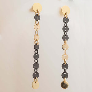 Pair of gold and black chain earrings on a light beige background