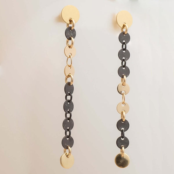 Pair of gold and black chain earrings on a light beige background