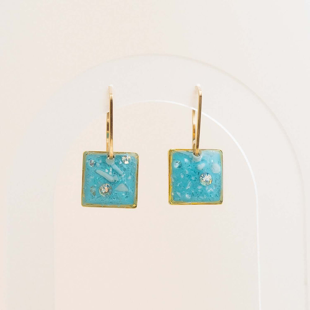 Pair of earrings with turquoise square stones and gold accents on a white background