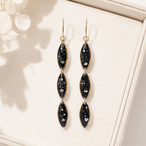 Pair of black and gold earrings on a beige surface with a soft background