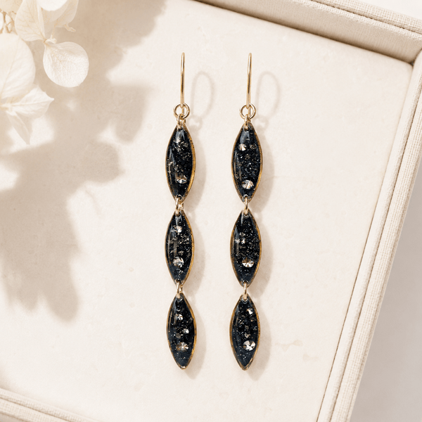 Pair of black and gold earrings on a beige surface with a soft background