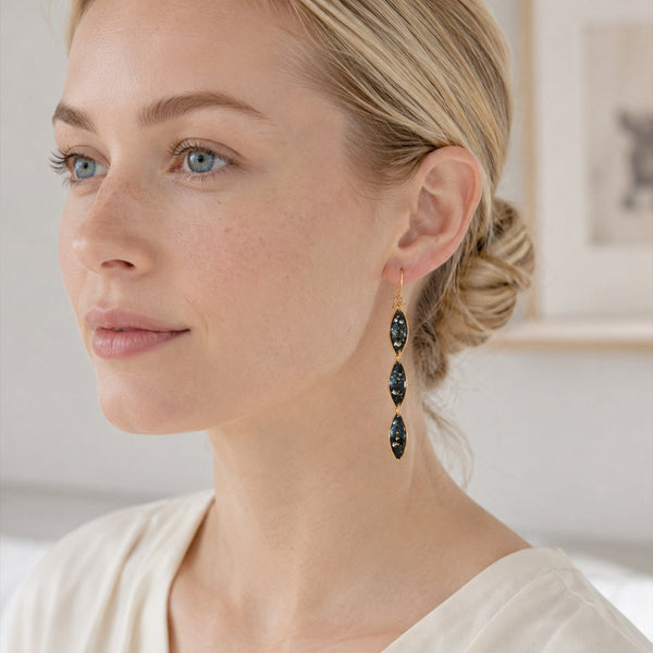 Woman wearing gold earrings with dark gemstones against a neutral background
