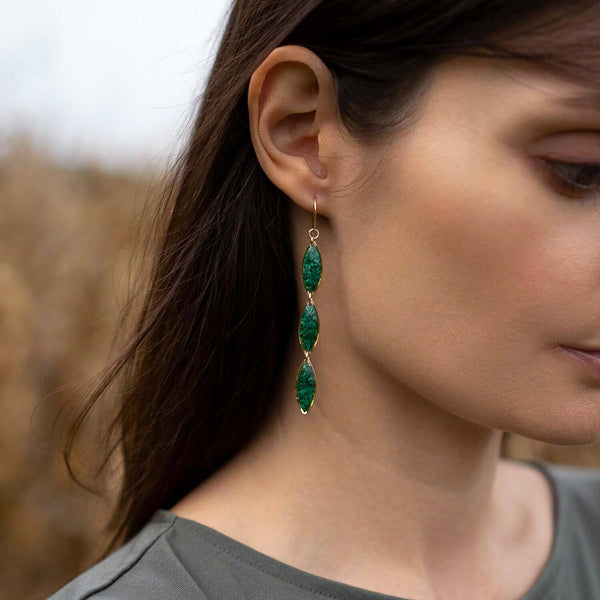 Close-up of a woman wearing emerald green earrings with a blurred natural background