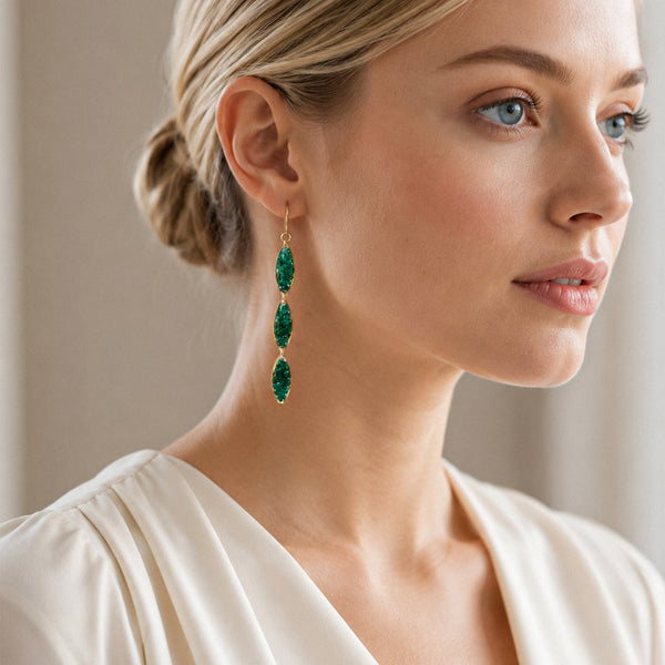Woman wearing green drop earrings with a neutral background
