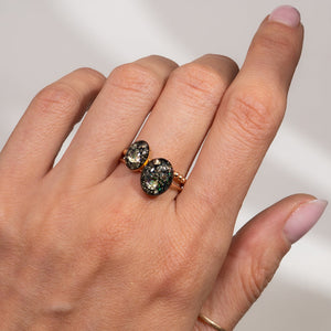 Hand wearing a ring with two dark gemstones on a neutral background
