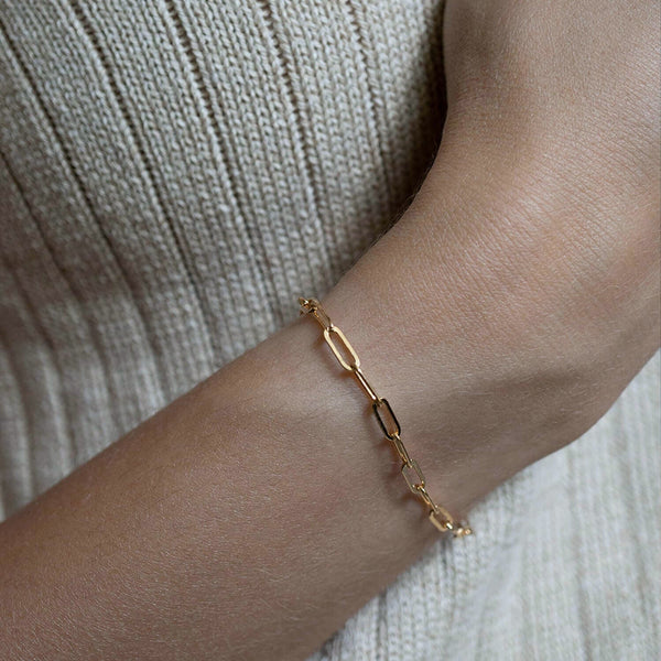 Gold chain bracelet on a wrist with a neutral background