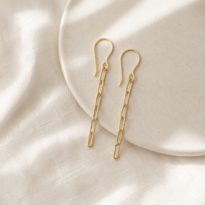 Gold chain earrings on a beige fabric background